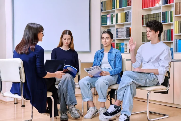 Psychology course Four young people sitting in a circle, engaged in discussion in a library setting about psychology principles.